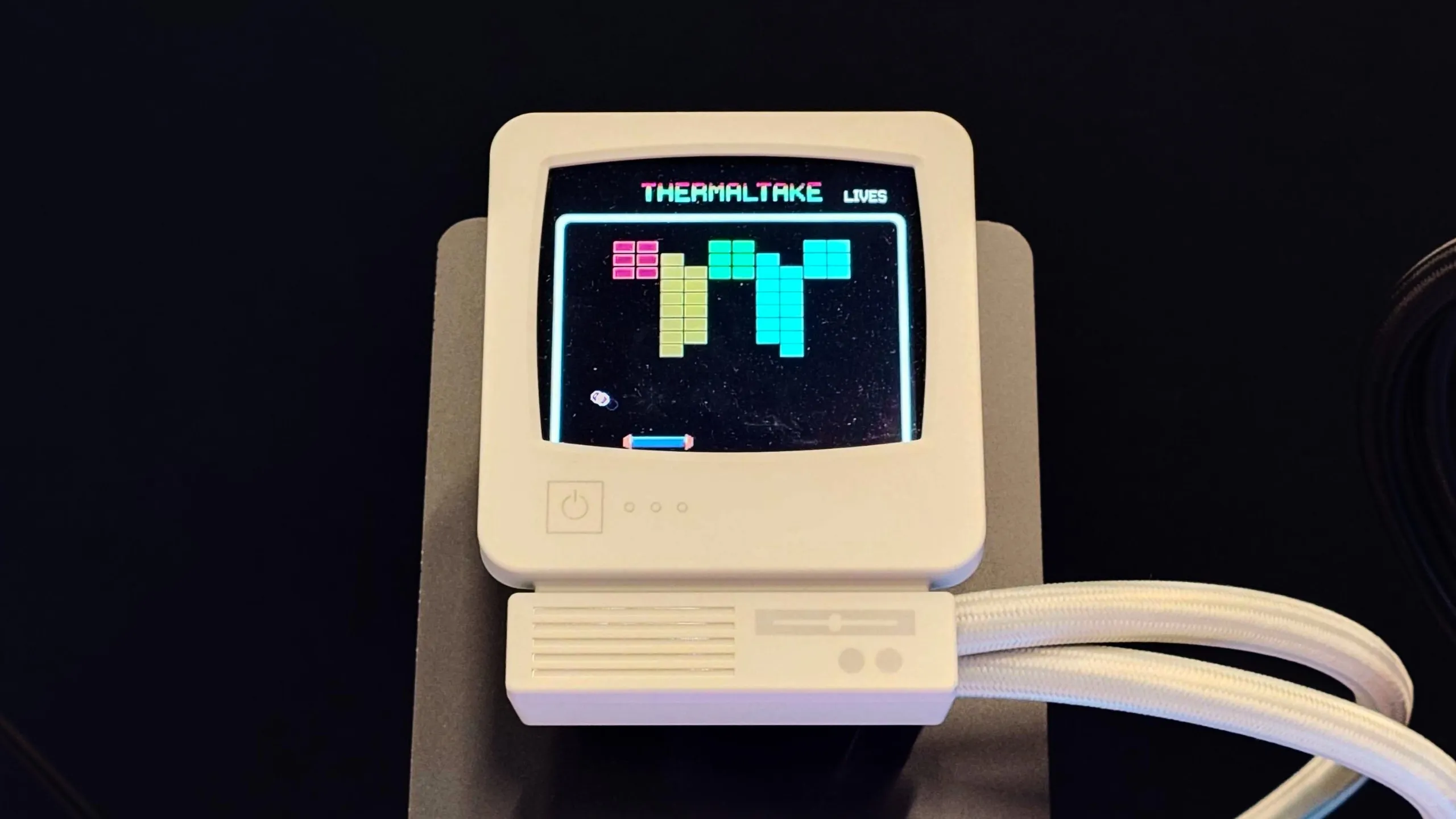 A photo of the Thermaltake Retro 360 AIO CPU cooler's CRT-style LCD display showing a block blaster type game