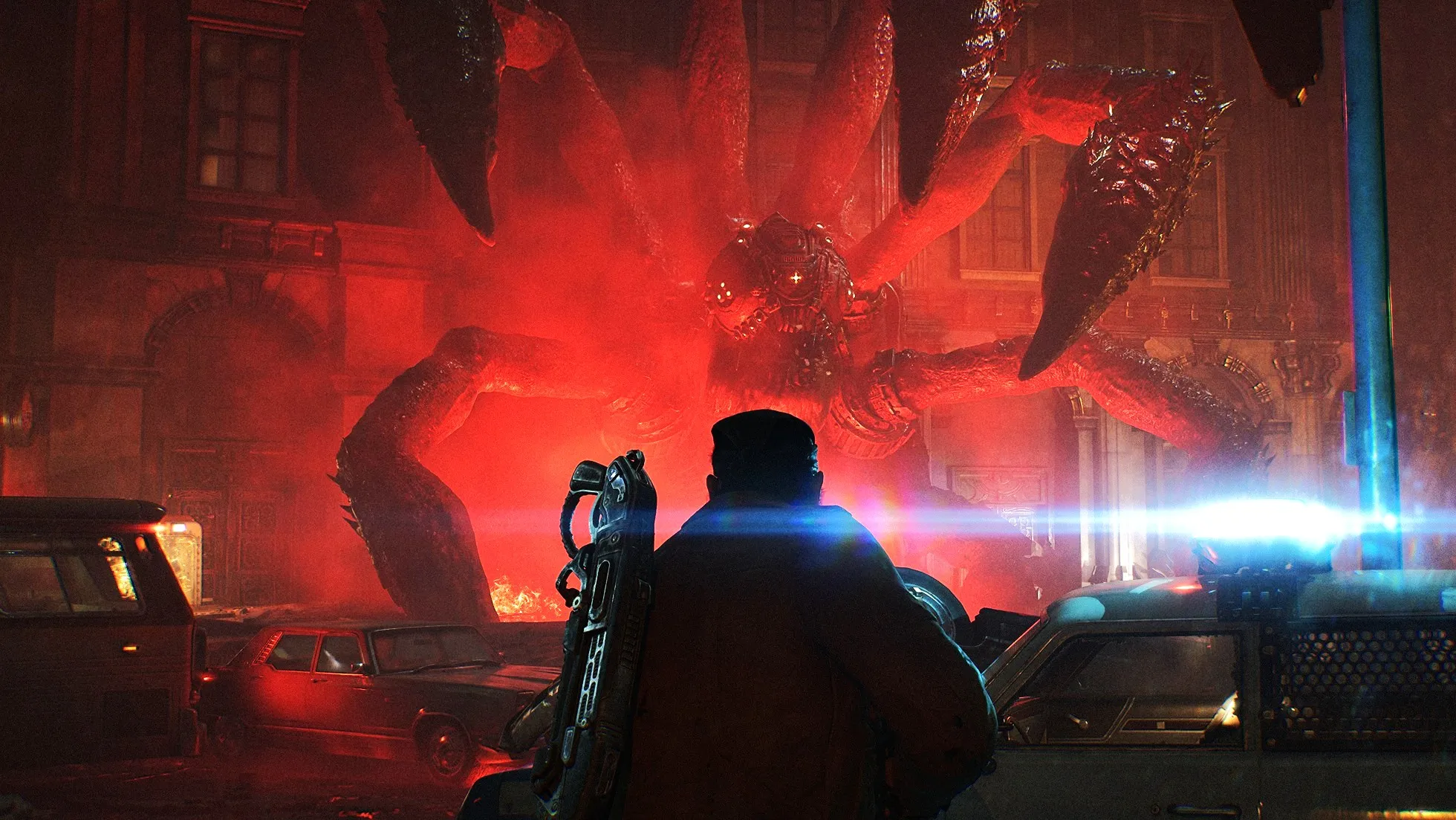 A lone armed figure faces a gigantic, many-limbed creature in a red-lit city street, with wrecked cars and a blue beam creating a tense, ominous scene.